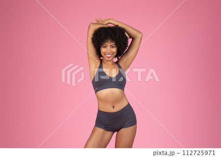 Joyful black woman in fitness attire stretching on pink background 112725971