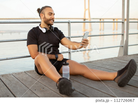 Sporty man with headphones checks fitness apps on phone outdoors Sporty man with headphones checks fitness apps on phone outdoors 112726067