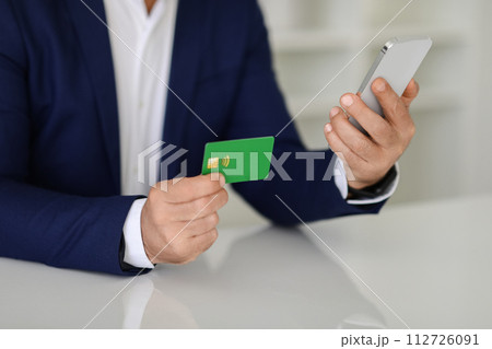 Close-up of a businessman's hands holding a green credit card and a smartphone 112726091
