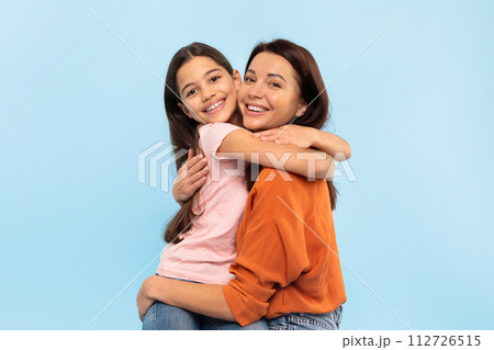 Happy Young Mom Hugging Her Little Daughter Over Blue Background Happy Young Mom Hugging Her Little Daughter Over Blue Background 112726515