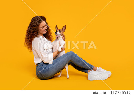 Curly-haired woman adoring her dog on yellow background Curly-haired woman adoring her dog on yellow background 112726537