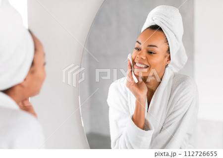Black millennial woman applying micellar water with cotton pad indoors 112726655