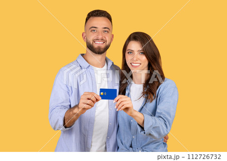 Smiling young couple holding credit card together Smiling young couple holding credit card together 112726732