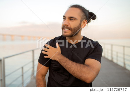 Man grimaces clutching his shoulder in discomfort after outdoor workout 112726757