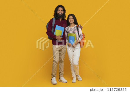 Positive eastern students friends posing on yellow background 112726825