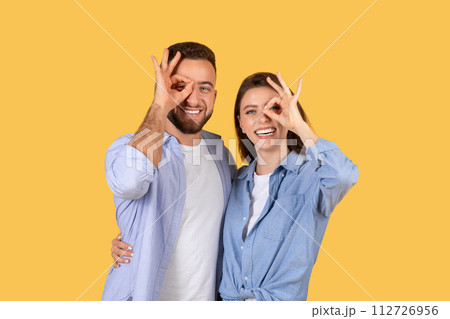 Playful european couple making fun gestures on yellow 112726956