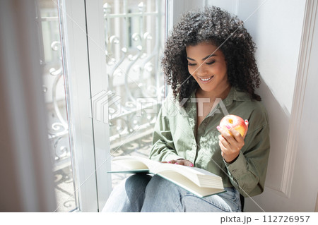 Happy Brazilian woman indulges in book reads by window indoors 112726957