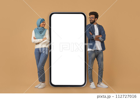 Happy young muslim couple leaning on giant smartphone with blank screen 112727016