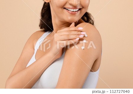 Indian woman with joyous smile delicately applying body lotion on her arm 112727040