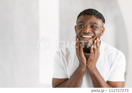 Young African American man smiles happily touching face in bathroom 112727273