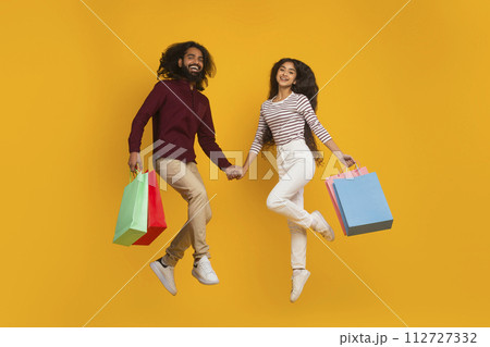 Emotional young indian couple jumping with shopping bags Emotional young indian couple jumping with shopping bags 112727332