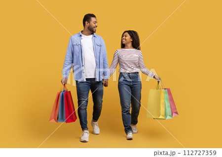 Smiling black couple carrying bright shopping bags, walking and holding hands Smiling black couple carrying bright shopping bags, walking and holding hands 112727359