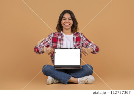 Happy middle eastern woman sit on floor, point at laptop Happy middle eastern woman sit on floor, point at laptop 112727367