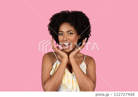 An exuberant young African American woman with curly afro hair joyfully holds her face An exuberant young African American woman with curly afro hair joyfully holds her face 112727488