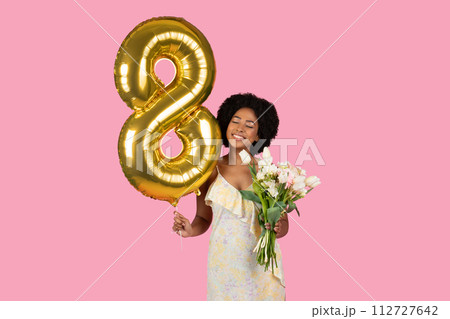 Happy African American woman with a natural hairstyle celebrating with a golden number 8 balloon Happy African American woman with a natural hairstyle celebrating with a golden number 8 balloon 112727642