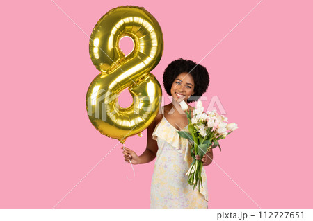 Joyful woman with curly hair celebrating with a golden number 8 balloon Joyful woman with curly hair celebrating with a golden number 8 balloon 112727651