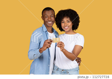 A cheerful young couple closely holds a gold credit card, sharing a moment of happy financial empowerment 112727728