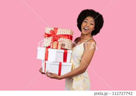 Excited African American woman with a beaming smile carrying a stack of gift boxes Excited African American woman with a beaming smile carrying a stack of gift boxes 112727742