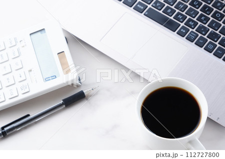 淹れたてのコーヒーを飲みながら、電卓とノートパソコンでデスクワークをしているイメージ 112727800