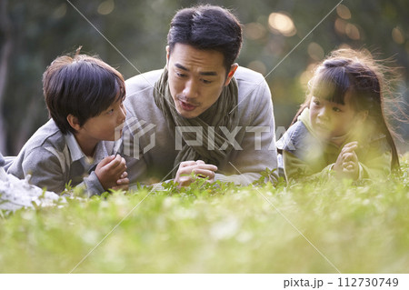 asian father and two children relaxing outdoors in city park asian father and two children relaxing outdoors in city park 112730749