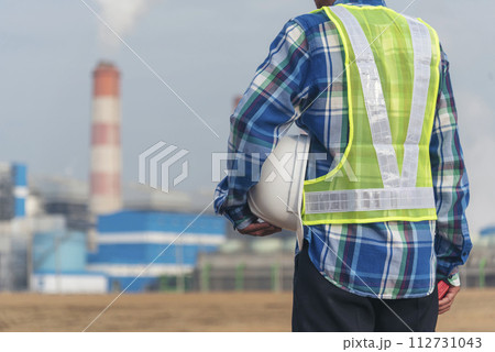 Backside Electrician engineer man hand holding White hardhat at Power stations manufacturing electrical plant. Technician worker blue hardhat helmet Engineer with steam smokestack industry background Backside Electrician engineer man hand holding White hardhat at Power stations manufacturing electrical plant. Technician worker blue hardhat helmet Engineer with steam smokestack industry background 112731043