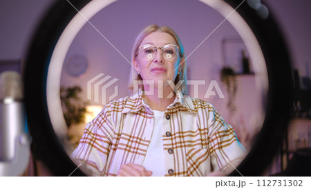 A mature woman blogger is adjusting a ring lamp before streaming online, utilizing modern devices 112731302
