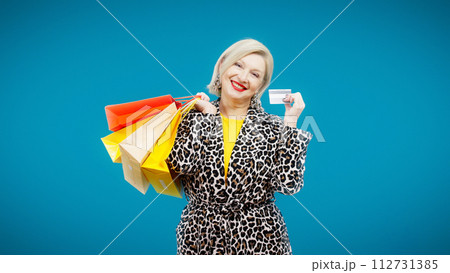 A happy senior woman with shopping bags is showing her credit card for online payment 112731385