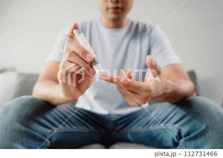 A man is sitting on a couch and holding a blood sugar testing device 112731466