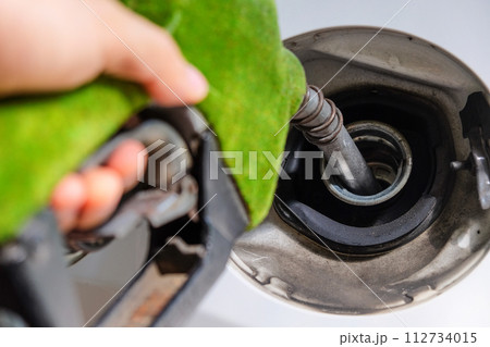 hand refilling a car with fuel at a gas station 112734015