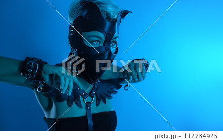 portrait of a hot sexy girl in a leather cat mask and muzzled in bdsm handcuffs on neon blue light portrait of a hot sexy girl in a leather cat mask and muzzled in bdsm handcuffs on neon blue light 112734925
