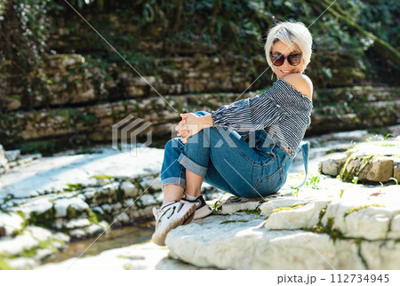 a beautiful sexy girl in nature among a mountain river and a rocky canyon in a denim jumpsuit smiles cheerfully and enjoys life on vacation in the summer 112734945