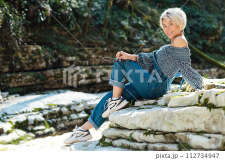 a beautiful sexy girl in nature among a mountain river and a rocky canyon in a denim jumpsuit smiles cheerfully and enjoys life on vacation in the summer 112734947