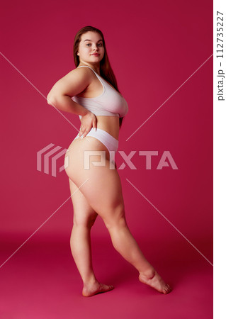 Young attractive, confident woman posing in white lingerie, bikini looking away against vibrant pink studio background. Young attractive, confident woman posing in white lingerie, bikini looking away against vibrant pink studio background. 112735227