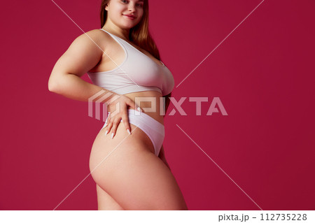 Cropped portrait of woman, model plus size posing in lingerie against pink studio background. Overweight girl looks confident. Cropped portrait of woman, model plus size posing in lingerie against pink studio background. Overweight girl looks confident. 112735228