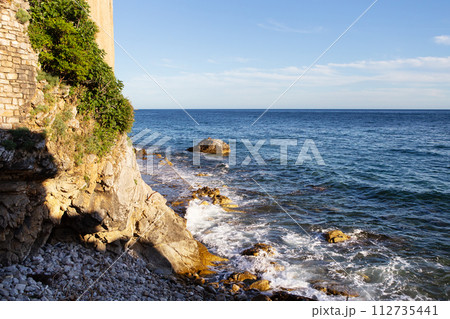 A tranquil seascape with rocky shores, lush greenery, and a clear blue sky. A tranquil seascape with rocky shores, lush greenery, and a clear blue sky. 112735441
