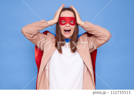 Unhappy displeased woman wearing superhero costume standing isolated over blue background crying with despair holding head suffering having bad feelings Unhappy displeased woman wearing superhero costume standing isolated over blue background crying with despair holding head suffering having bad feelings 112735513