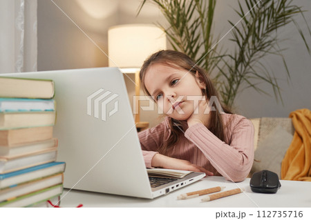 Online learning resources for children. Digital education platforms for kids. Tired sad little girl using laptop while sitting at table at home suffering neck pain Online learning resources for children. Digital education platforms for kids. Tired sad little girl using laptop while sitting at table at home suffering neck pain 112735716