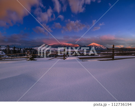 Alpine village outskirts in last evening sunset sun light. Winter snowy hills and fir trees. 112736194