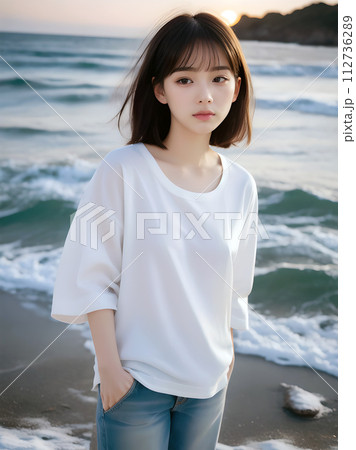 夕暮れの浜辺にたたずむ白Tシャツジーパンの若い女性 112736289