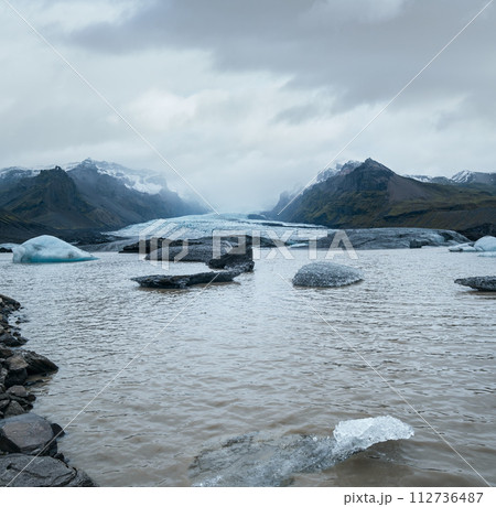 Glacier tongue slides from Vatnajokull icecap or Vatna Glacier, Iceland. Glacial lagoon with ice blocks and surrounding mountains. 112736487