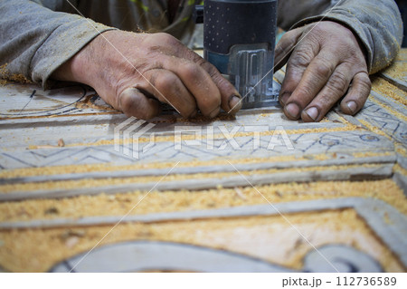 Close Up of Man Hands carving on wooden furniture. Carpenter using tool making Artistic Wood Carving. Producing an Ornament on Wood with Chisel and Hammer on a Panel of Wood . High quality photo 112736589