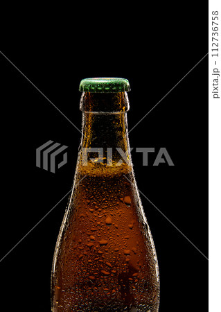 Close-up of brown beer bottle with green cap against black background. Bubbles lager foamy beer 112736758