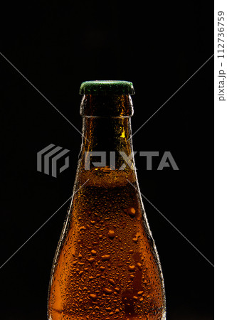 Close-up of brown beer bottle with green cap against black background. Bubbles lager foamy beer 112736759