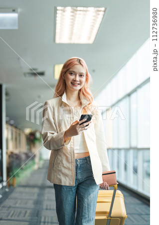 Traveler woman asian in airport and luggage for vacation, smile and holding the phone check boarding ticket. Female traveler with suitcase, international and departure with passport and trip Traveler woman asian in airport and luggage for vacation, smile and holding the phone check boarding ticket. Female traveler with suitcase, international and departure with passport and trip 112736980