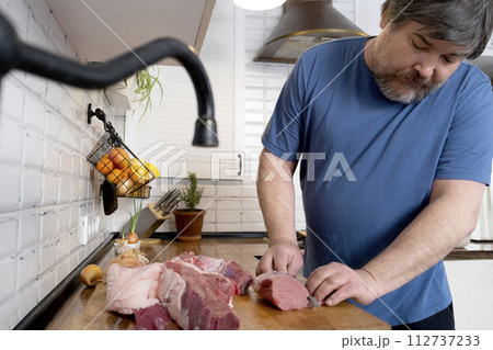 Real men cutting fresh raw meat on board in white kitchen. Preparing pork meat, cooking Real men cutting fresh raw meat on board in white kitchen. Preparing pork meat, cooking 112737233