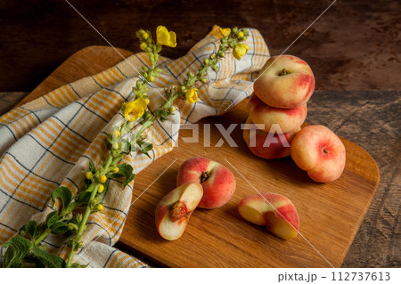Cutting board with halves and several whole saturn peaches or flat peaches on wooden background with yellow kitchen towel.. Cutting board with halves and several whole saturn peaches or flat peaches on wooden background with yellow kitchen towel.. 112737613