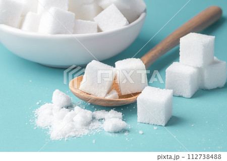 Sugar cube on wood spoon, closeup on blue background 112738488