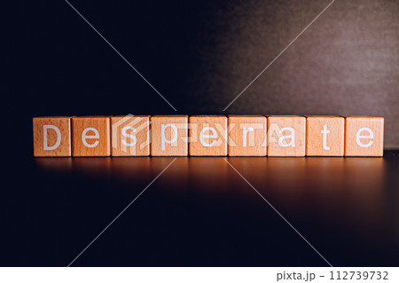 Wooden blocks form the text "Desperate" against a black background. 112739732