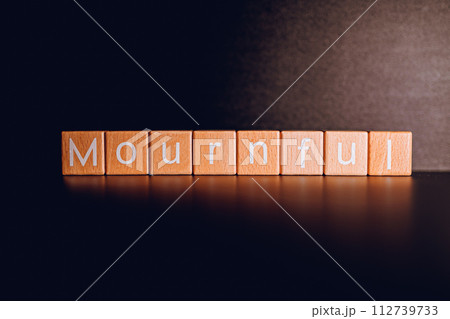 Wooden blocks form the text "Mournful" against a black background. 112739733
