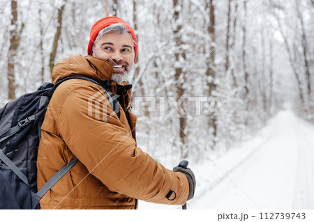 Man having a walk with scandinavian sticks in a snowy forest Man having a walk with scandinavian sticks in a snowy forest 112739743